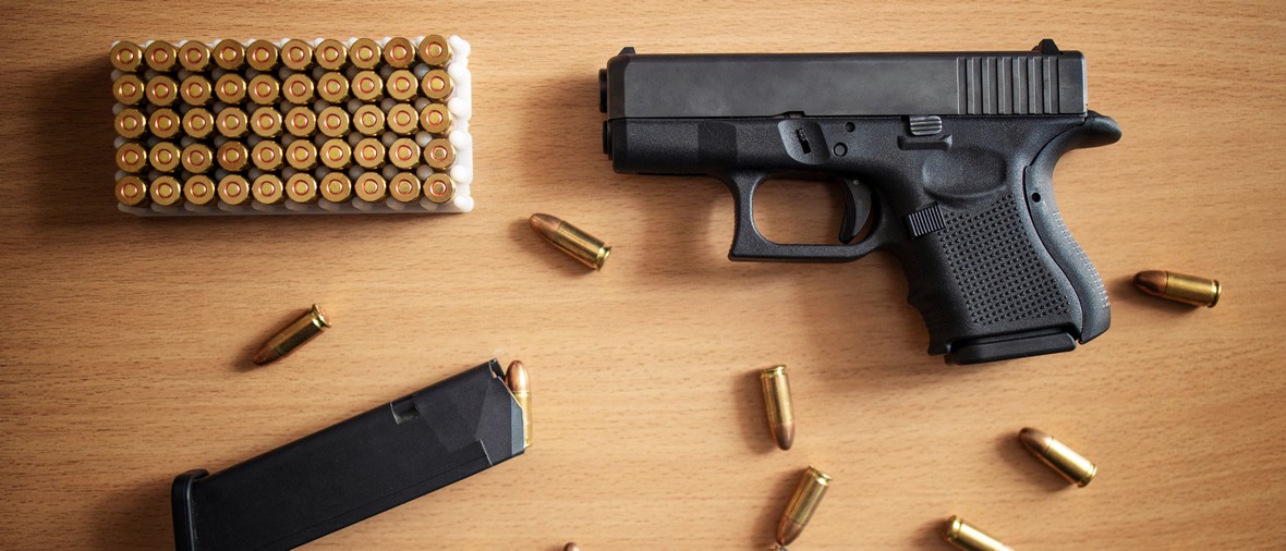 Gun with box of ammunition and bullets on wooden background.
