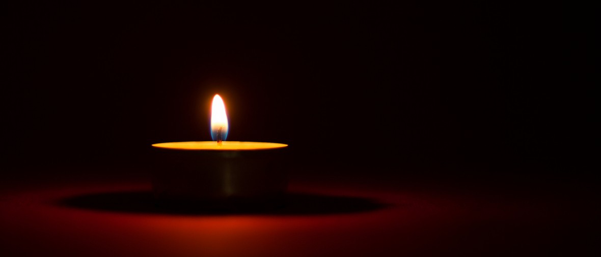 One candle burning in the dark, black and red background