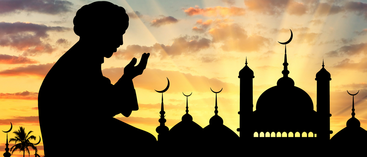 Concept of the Islamic religion. Silhouette of man praying on the background of the town hall at sunset