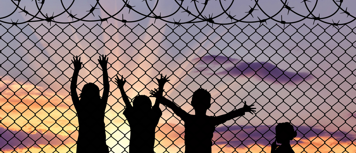 Concept of refugee. Silhouette of the hungry children of refugees near the border fence in the sunset